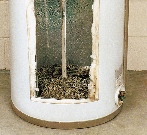 Close-up image of a water heater with its lower access panel removed, revealing a significant buildup of mineral deposits, indicative of hard water issues